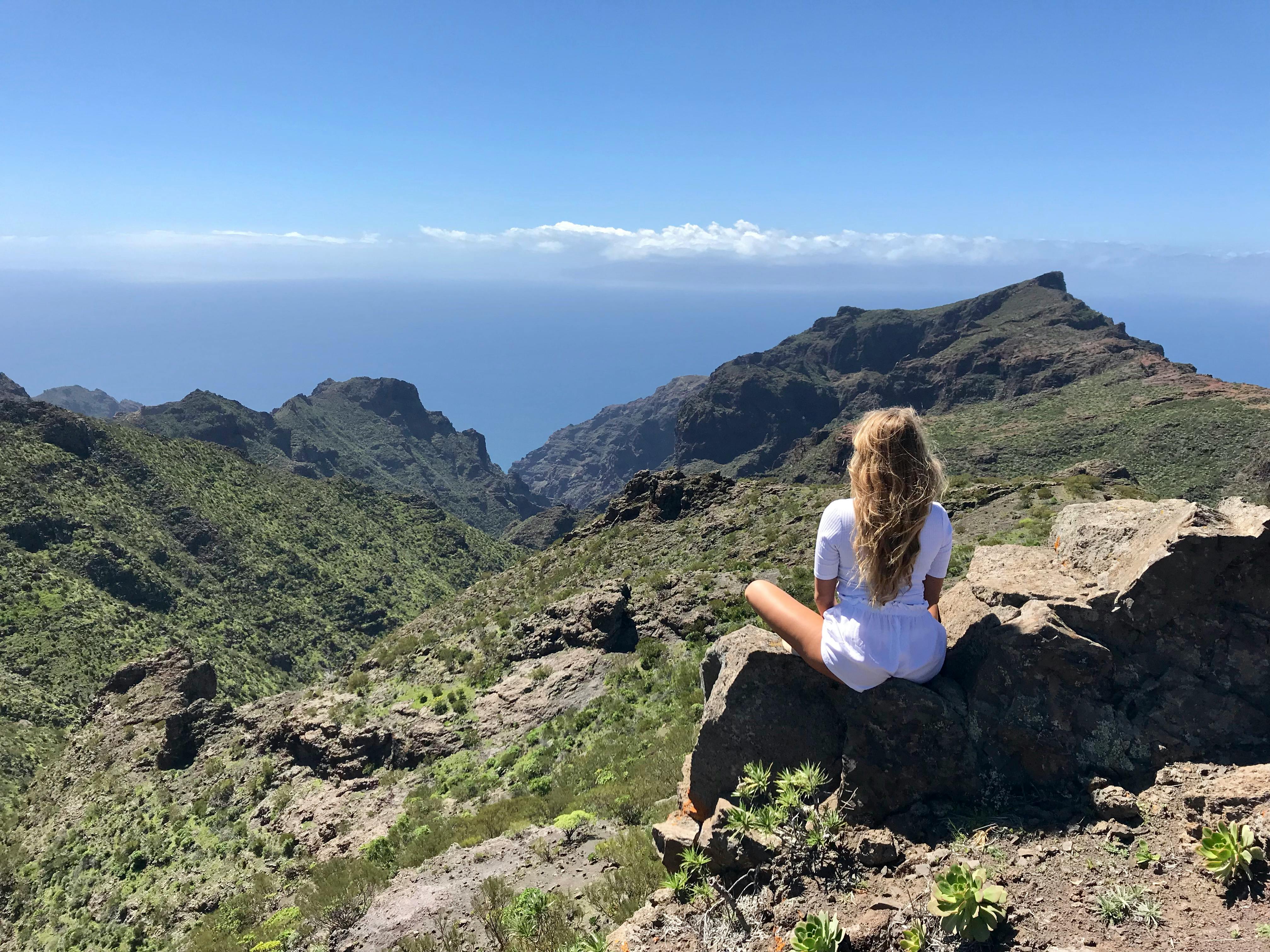 一个女人坐在岩石上，俯瞰着蓝天下的广阔山景