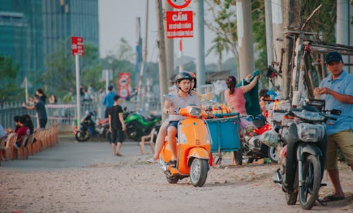 Man Wearing Grey Shirt Riding on Orange Motor Scooter at Daytime