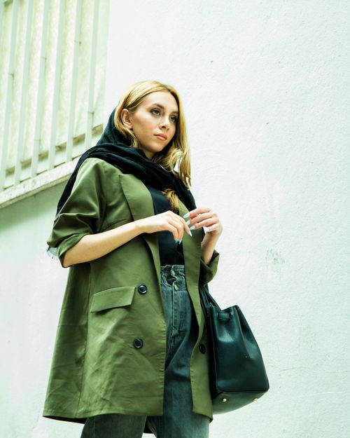 Free Fashionable young woman in olive coat and scarf posing outdoors. Urban chic vibe. Stock Photo
