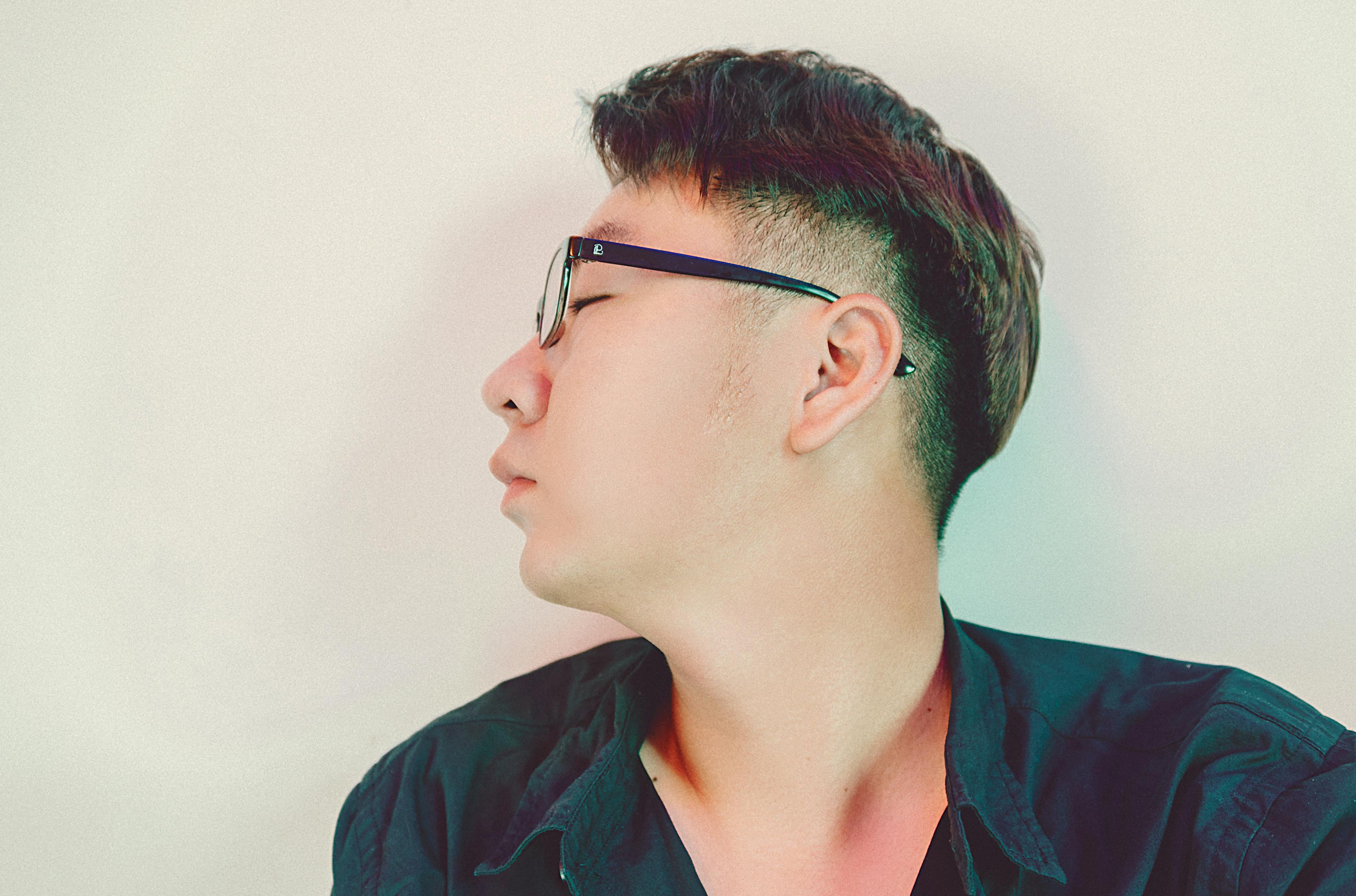Close-up side view of a young man wearing glasses against a neutral background.