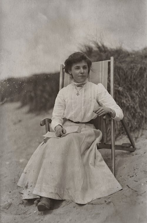 Grayscale Photo of Girl in Dress Sitting on a Chair