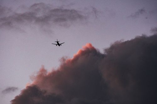 Free Silhouette of an airplane flying against a dramatic cloudy sky during twilight. Stock Photo