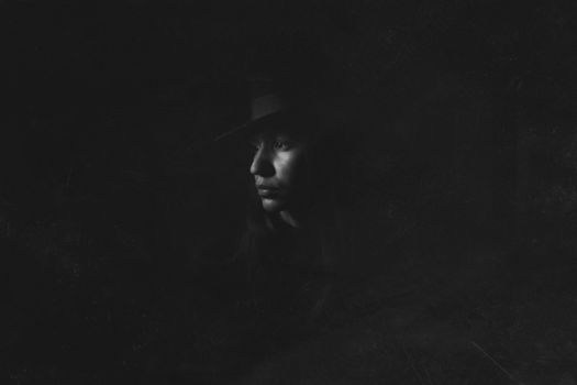 Dramatic black and white portrait of a woman wearing a hat in shadows.
