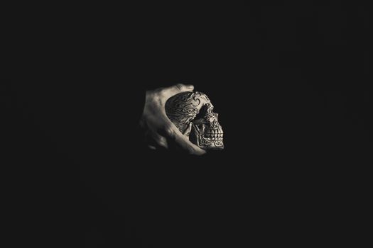 An artistic monochrome image of a hand holding a detailed skull against a dark background, emphasizing texture and form.