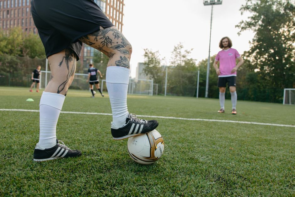 Close-up of a soccer player with tattoos controlling the ball on an outdoor field during practice.