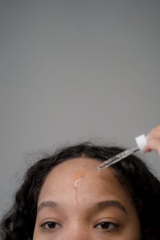 Woman applying skincare serum on forehead for hydration.