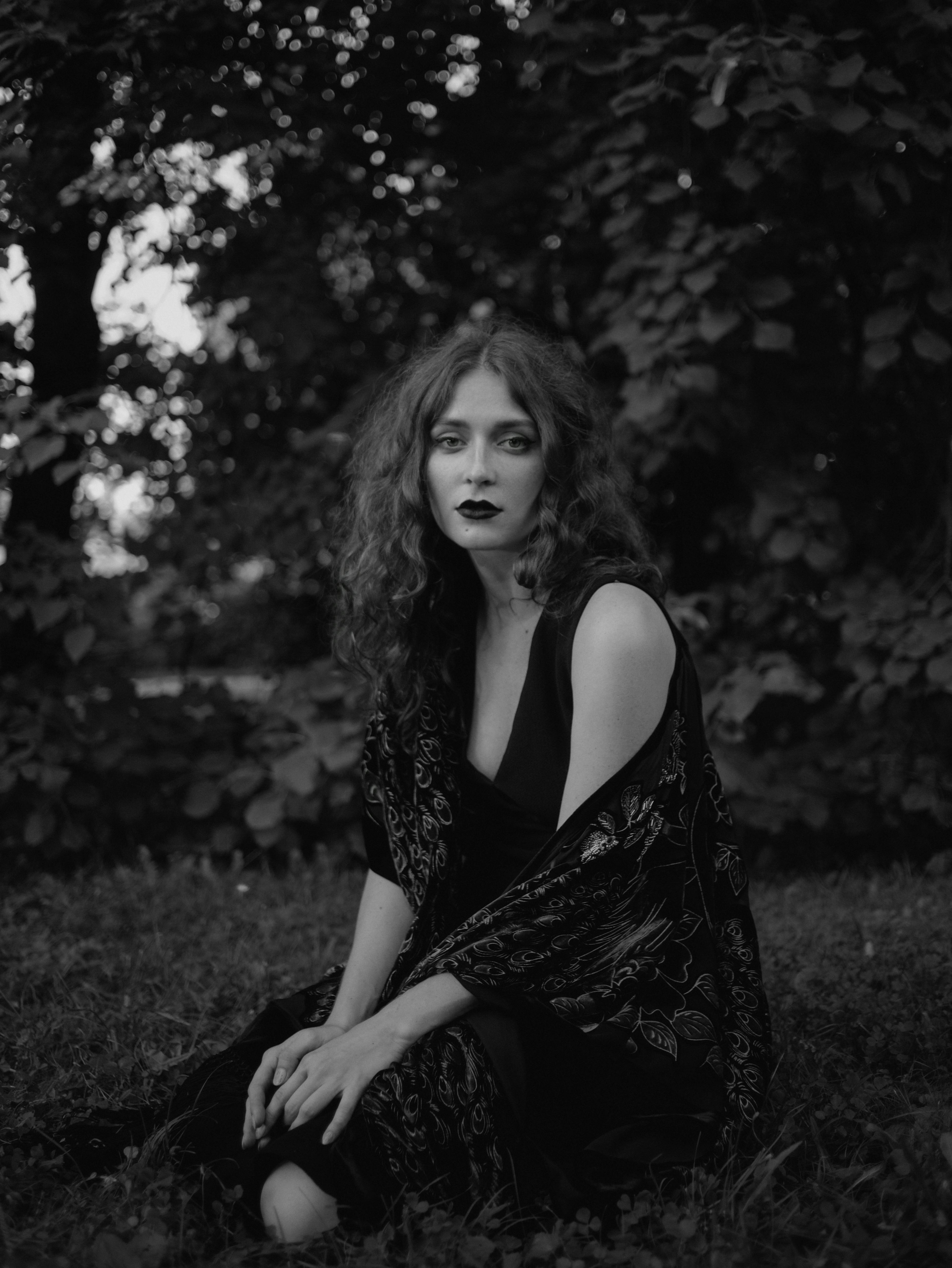 A contemplative woman in nature captured in grayscale, embodying elegance and mystery.