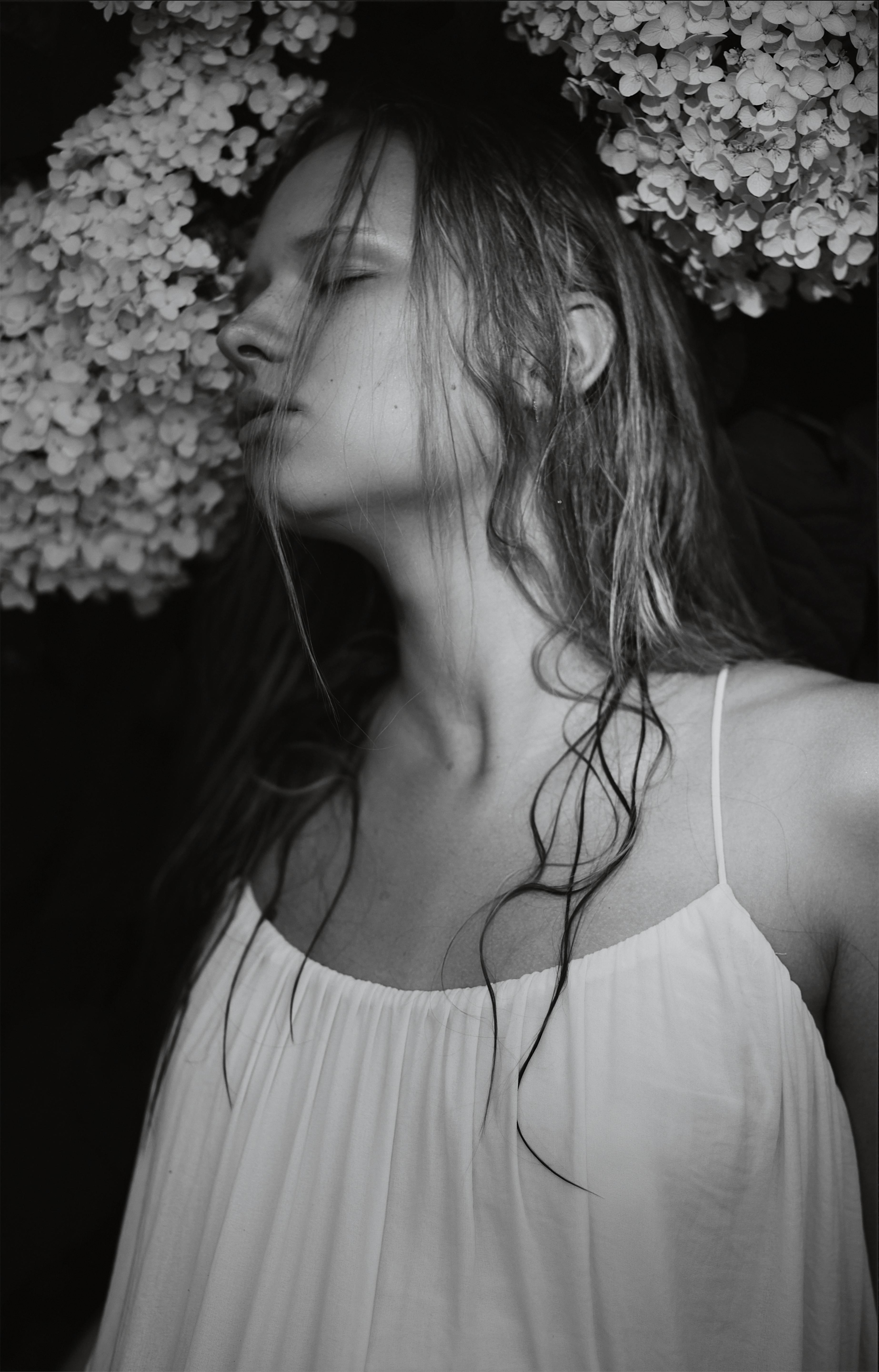 A contemplative portrait of a woman in grayscale with flowers surrounding her.