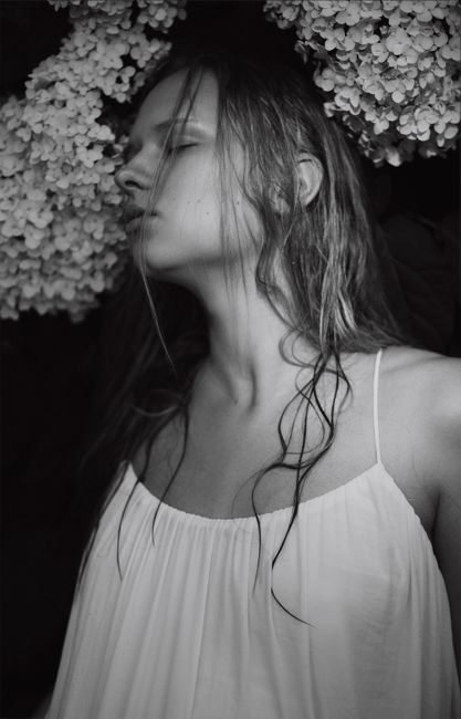 A contemplative portrait of a woman in grayscale with flowers surrounding her.