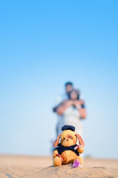阳光明媚的日子里，沙滩上的毛绒玩具前有一对模糊的情侣作为背景