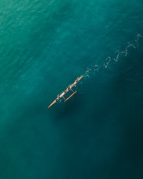 A top-down view of a canoe with people paddling on the teal ocean waters of Rio de Janeiro.