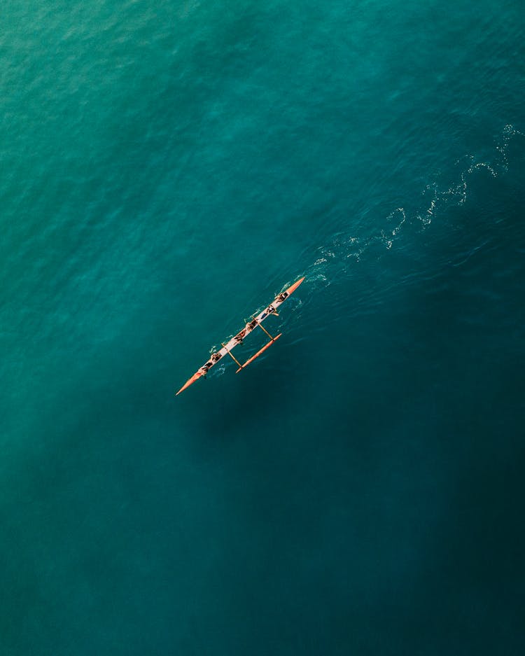 People Paddling An Outrigger Canoe In The Blue Ocean