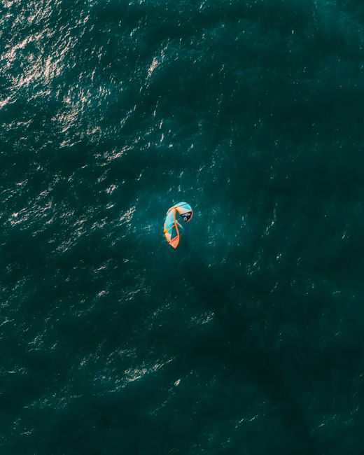 Aerial shot of a windsurfer navigating the vast ocean near Rio de Janeiro, Brazil, showcasing vibrant waters and dynamic motion.