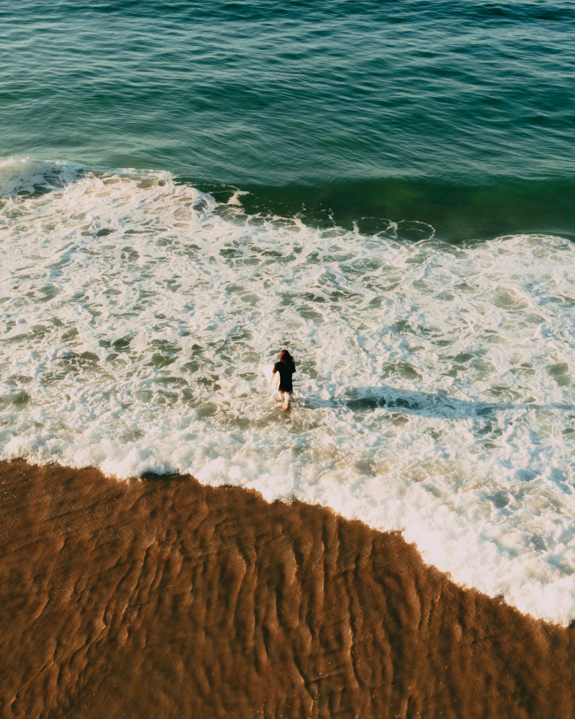 person in black jacket and black pants standing on brown sand near body of water during