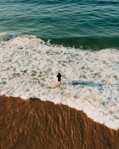 Free A person walks into waves on a beach in Rio de Janeiro, caught from above and behind, creating a breathtaking coastal scene. Stock Photo