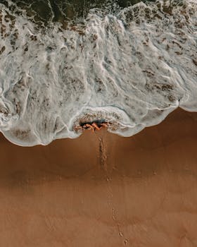 Aerial shot of a woman lying on Rio de Janeiro beach with waves crashing. Perfect for travel and lifestyle content.