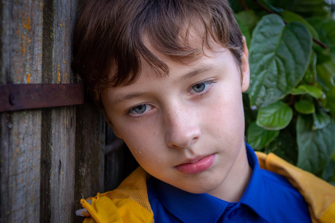 Close-Up Shot of a Young Boy Leaning on Wooden Wall · Free Stock Photo
