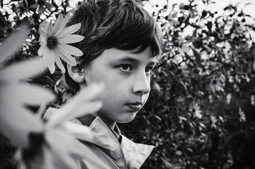 Grayscale Photo of a Boy Standing Near Plants