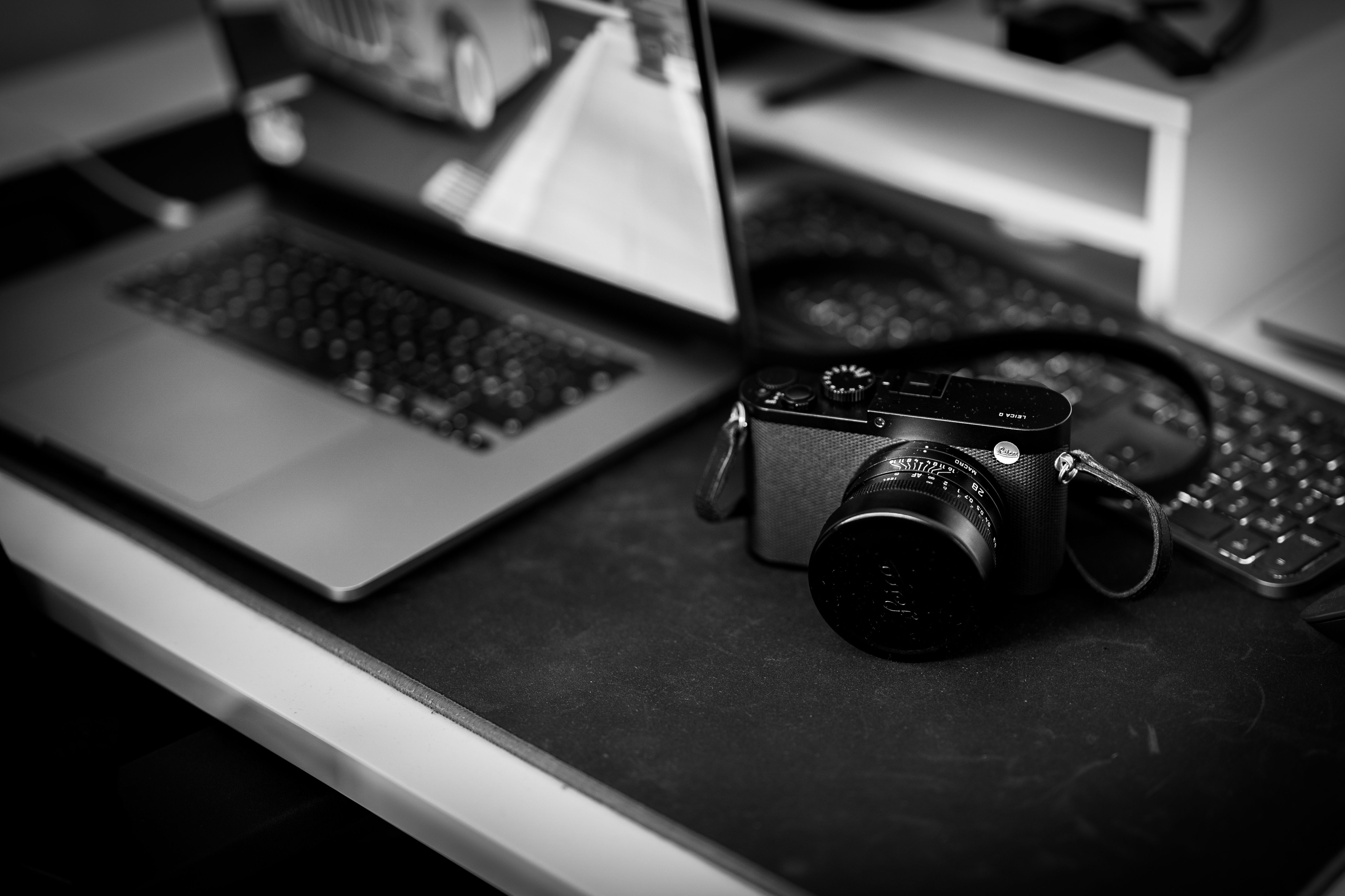 A vintage camera placed on a desk beside a laptop, in a black and white setting.