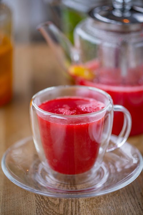 Free A vibrant red fruit drink in a clear glass cup with a teapot in the background. Stock Photo