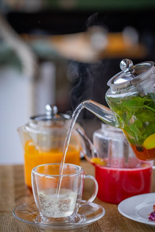 Free Close-up of herbal tea being poured into a glass cup on a wooden table with steam visible. Stock Photo