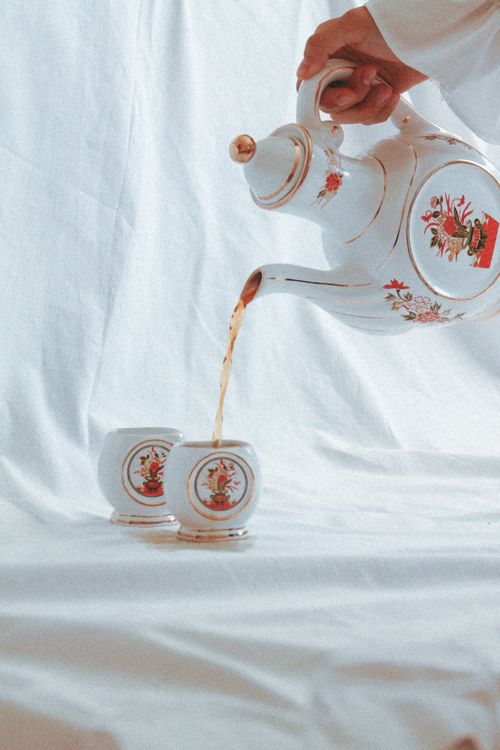 Free Close-up of a decorative teapot pouring hot tea into cups on a fabric backdrop. Stock Photo