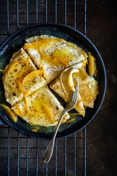 Indulge in golden crepes with fresh orange slices and syrup, perfect for breakfast.