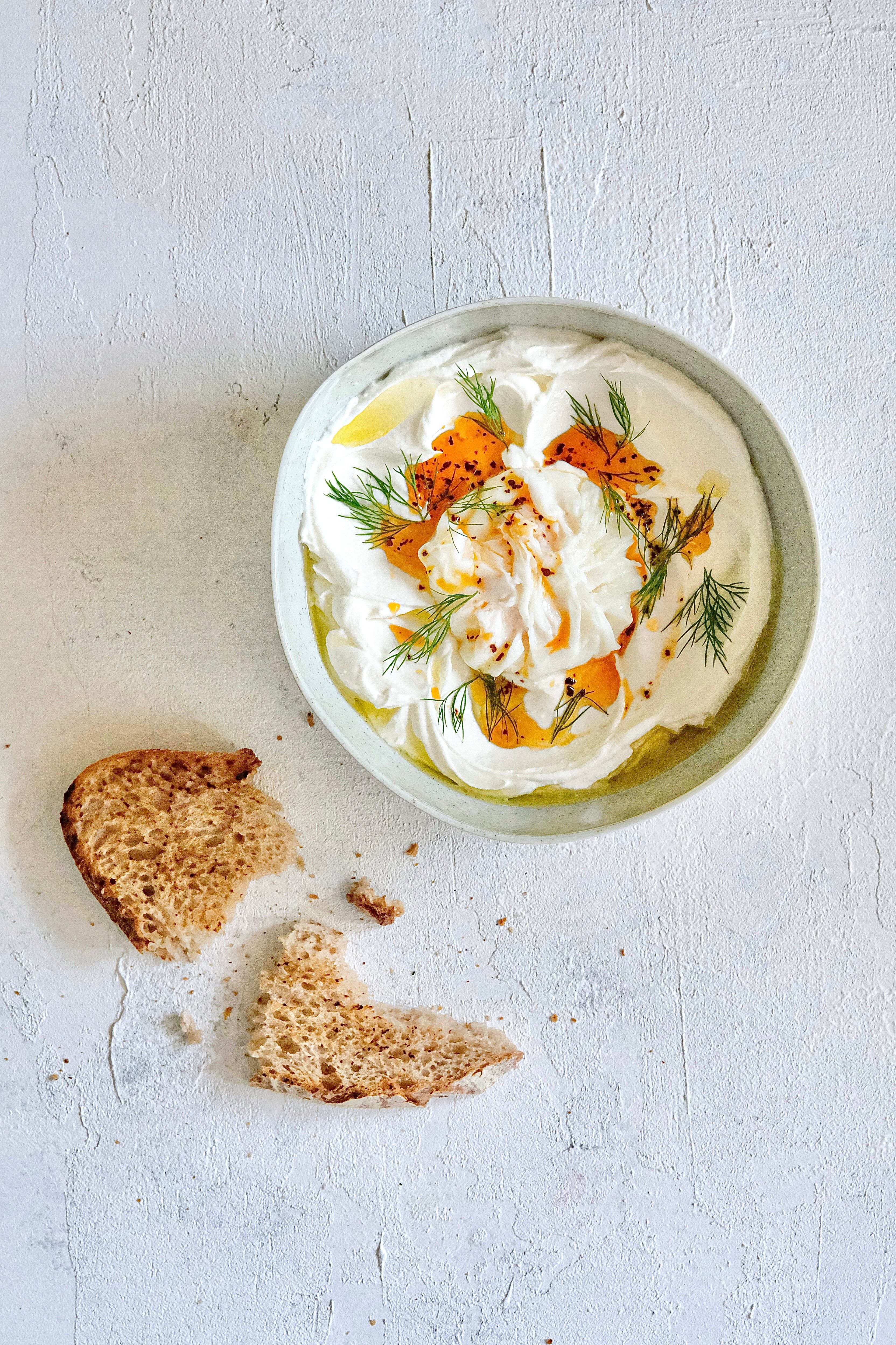 Top-down view of a healthy yogurt bowl with herbs and bread on a textured surface.