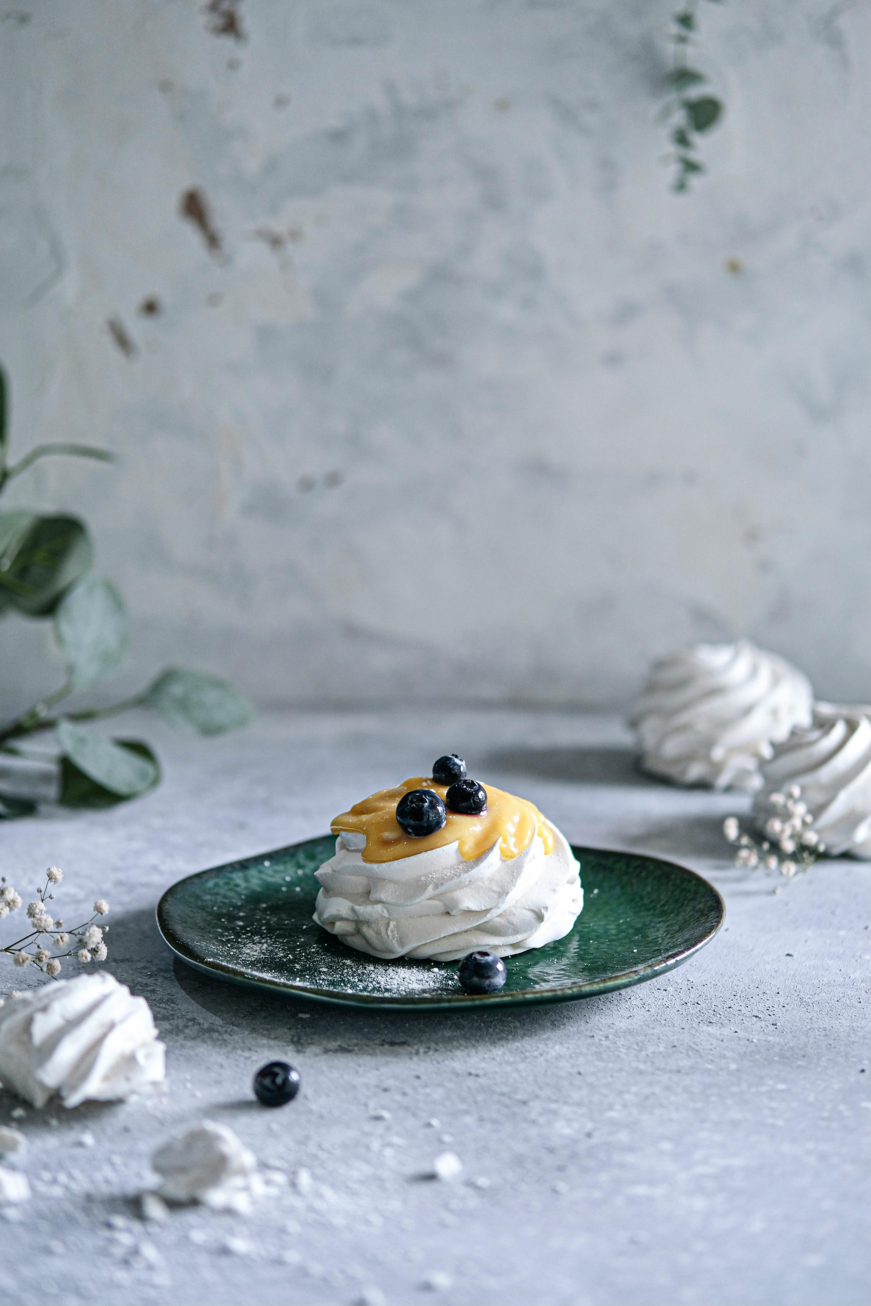 A meringue dessert topped with fresh blueberries and mango on a green plate, elegantly styled.