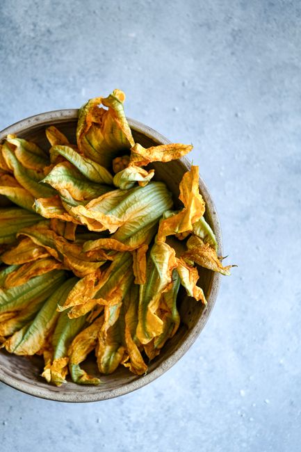 Bright yellow squash blossoms arranged in a wooden bowl on concrete background.