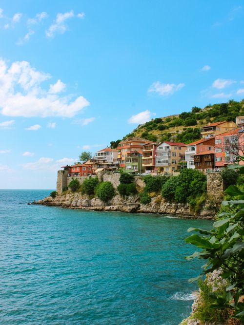 Free Charming coastal village with colorful houses perched on a cliff overlooking the turquoise sea under a clear blue sky. Stock Photo