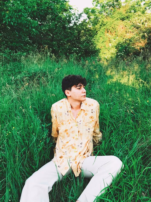 Man in Yellow Floral Button Up Shirt Sitting on Green Grass Field
