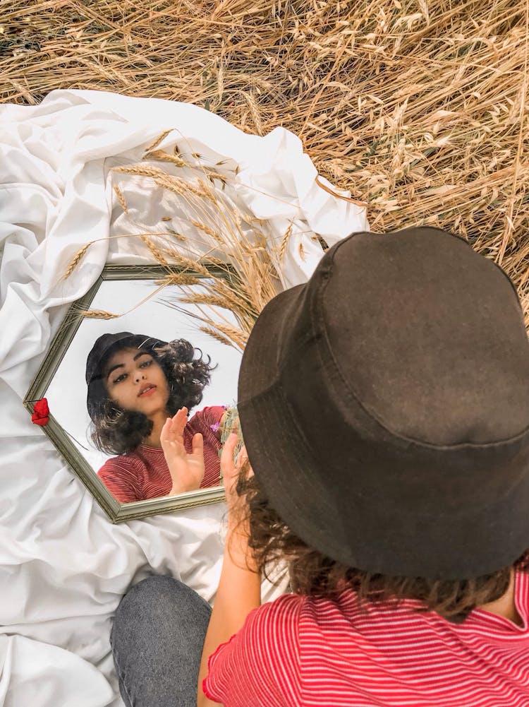 
A Woman Wearing A Hat Looking At A Mirror