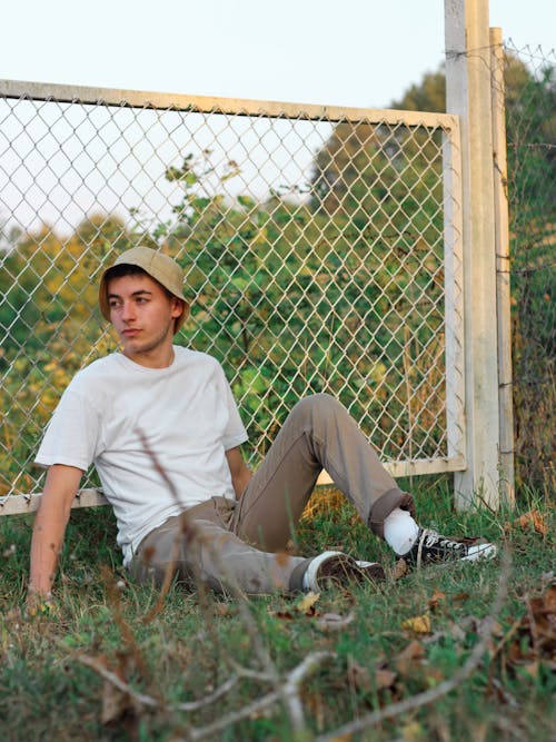 Man in a White Crew Neck Shirt Sitting Near a Chain Fence