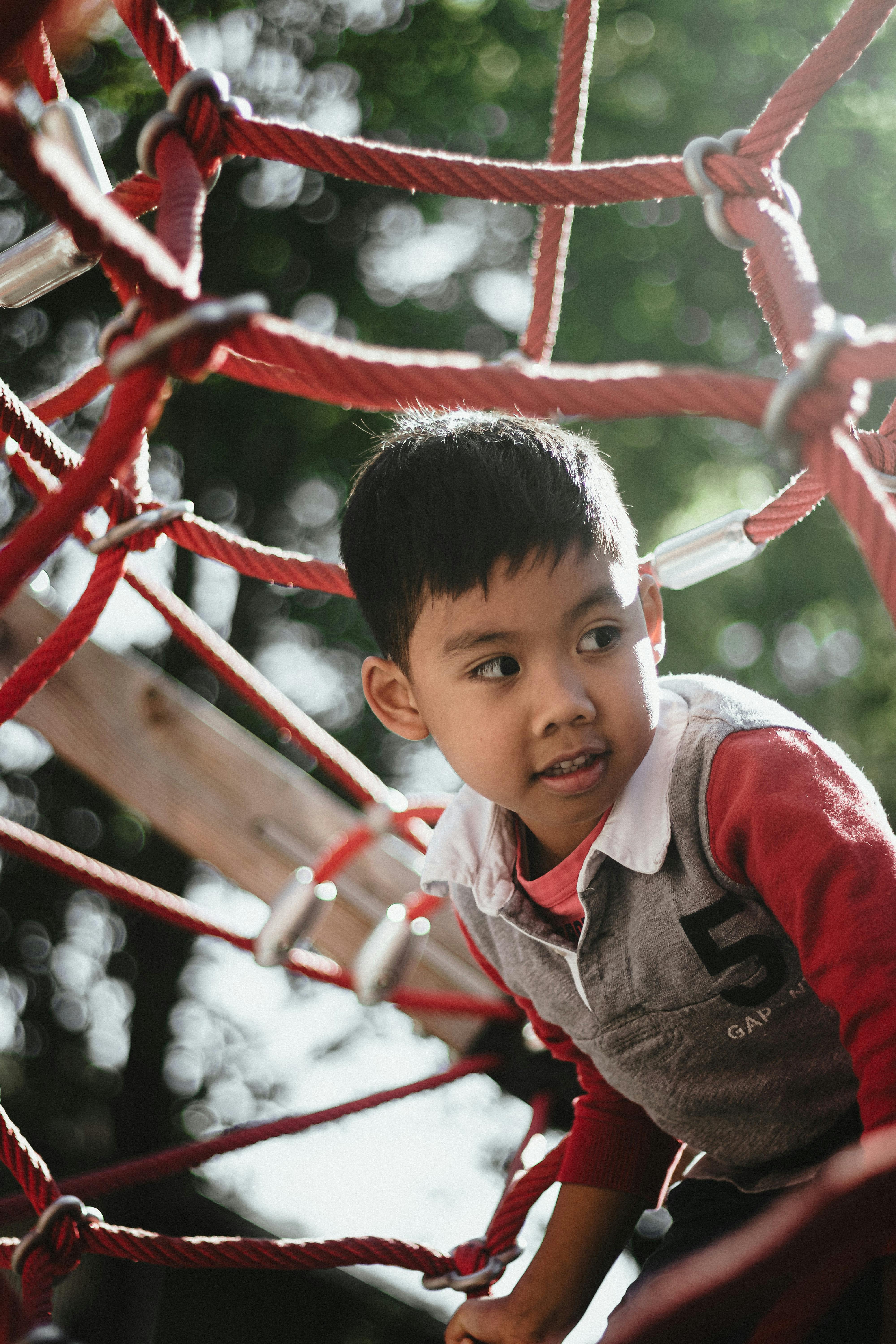 A child climbing on red rope structures in an outdoor playground setting.