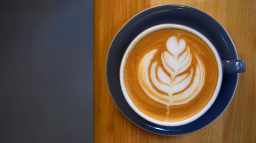 Free Close-up of a latte with artistic foam design on a wooden table. Stock Photo