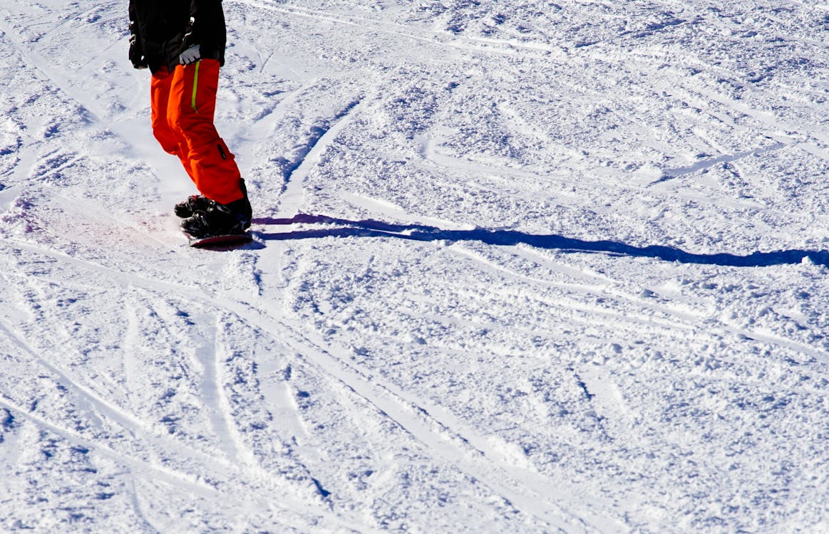 Foto Della Persona Che Indossa La Parte Superiore Nera E Pantaloni Arancioni Che Guida Lo Snowboard