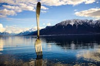 湖面上倒映着叉子雕塑，群山白雪皑皑，天空充满活力