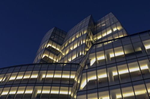 Free Low angle view of a modern glass building glowing at twilight, showcasing architectural beauty. Stock Photo