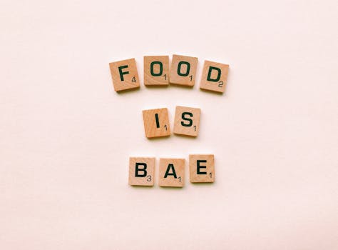 Scrabble tiles spelling 'Food is Bae' on a minimalist, textured background, emphasizing a playful message.