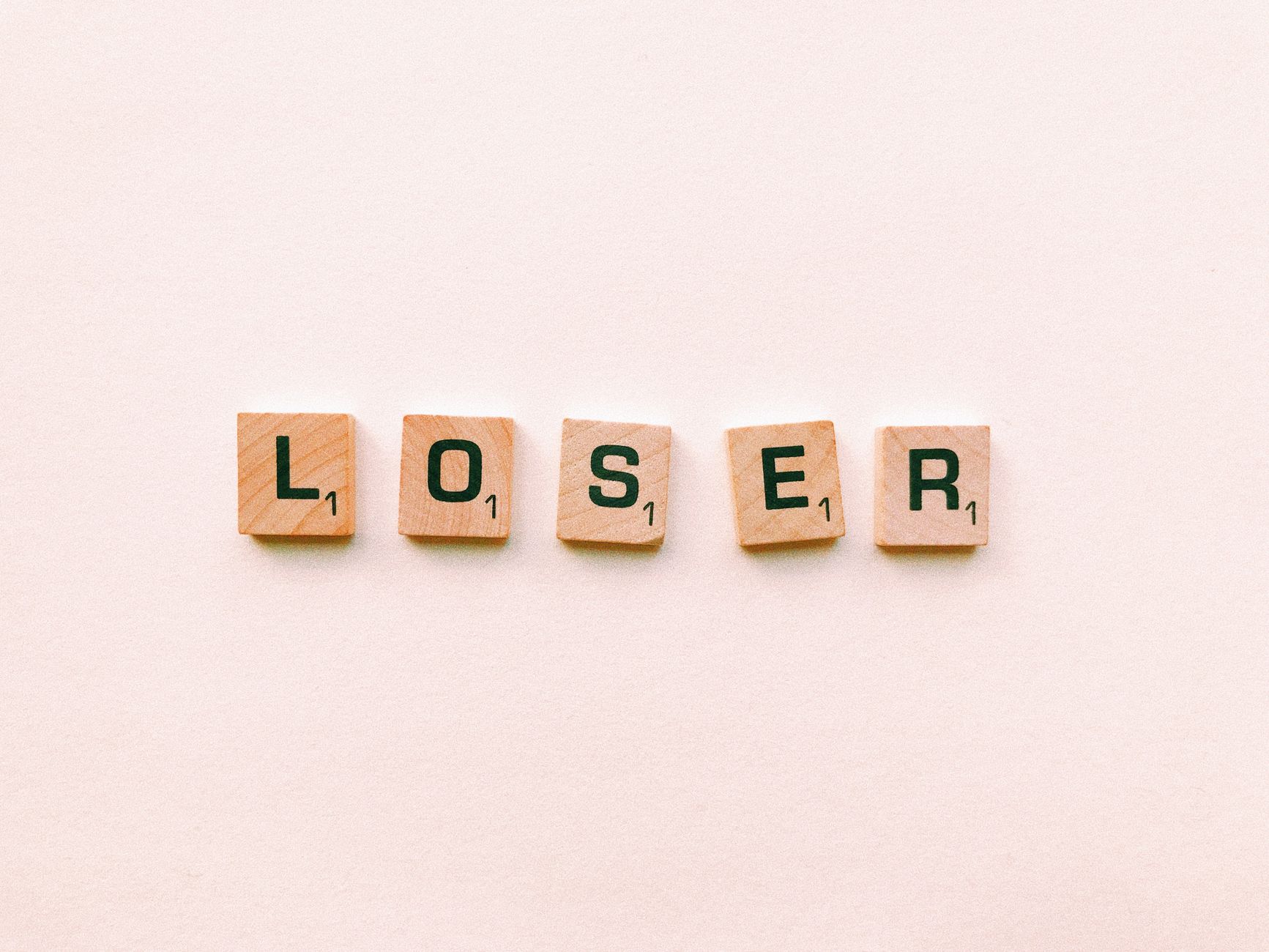 Five wooden tiles spell the word 'loser' in a minimalist and symbolic photo.