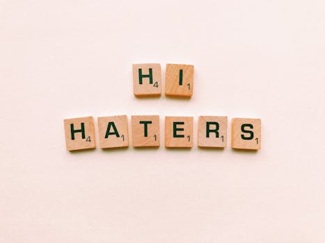 Wooden scrabble tiles spelling 'Hi Haters' on a light beige background.