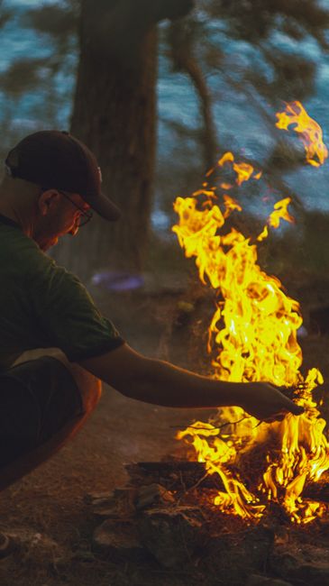 Fotomural Un hombre se agacha junto a una fogata rugiente en un bosque durante una tarde de verano.