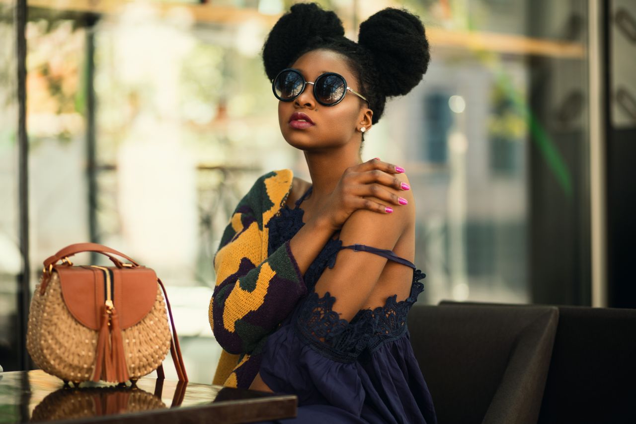 fashionable woman in a chic outfit and sunglasses sitting indoors with