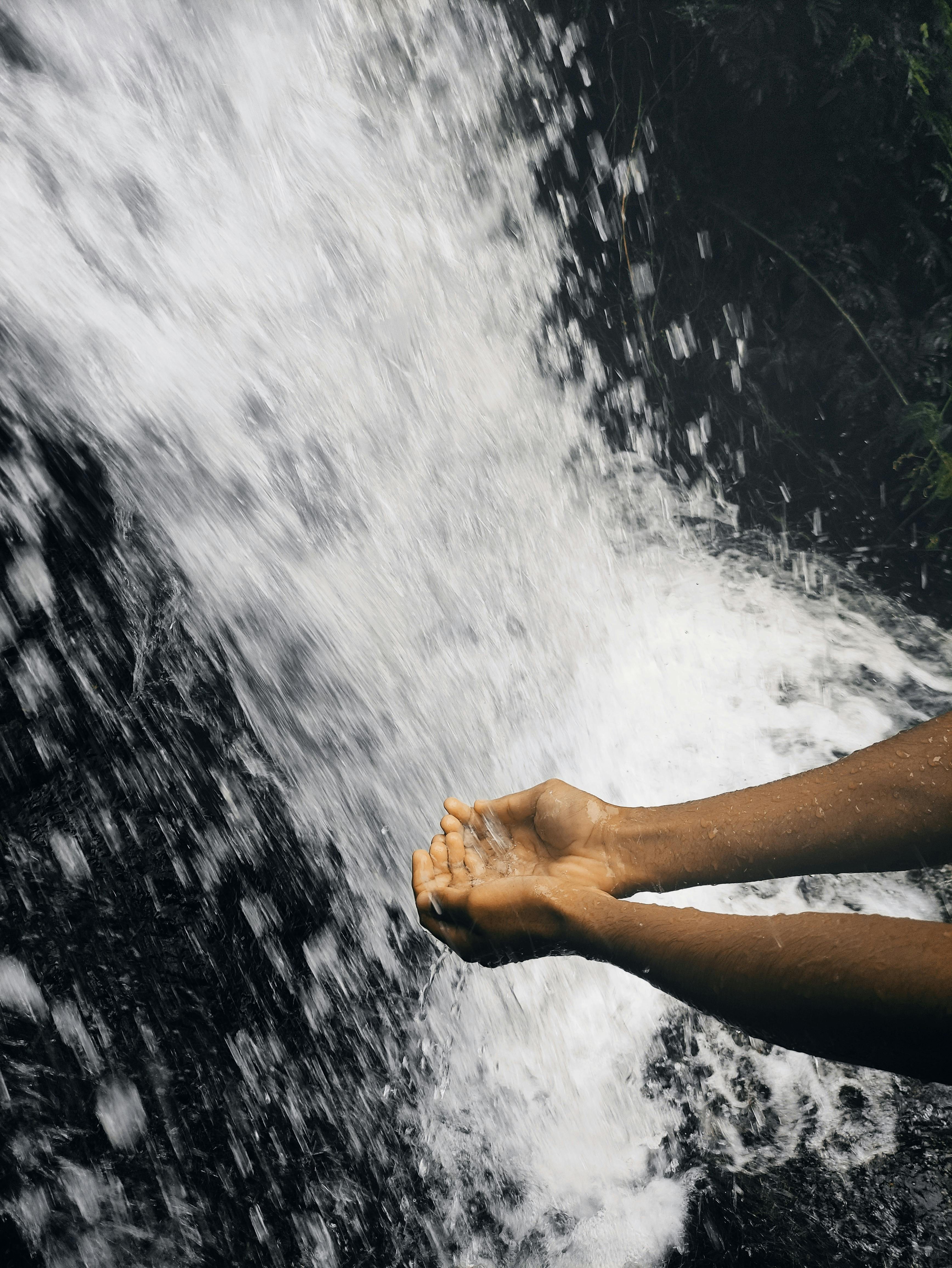 Close-up of hands enjoying the refreshing splash of a waterfall outdoors. Vibrant and natural.