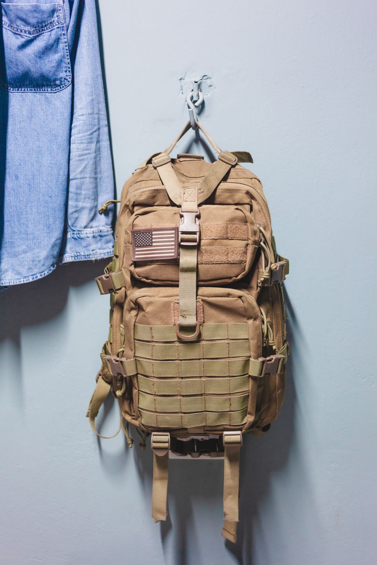 Backpack hanging on a wall hook next to a jacket in a small apartment entryway