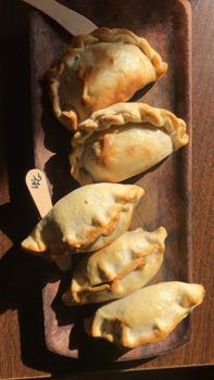 Delicious homemade empanadas served on a rustic wooden tray in warm lighting.
