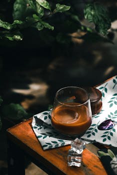 Close-up of iced coffee in glass on rustic table with natural light and leafy backdrop in Nha Trang.