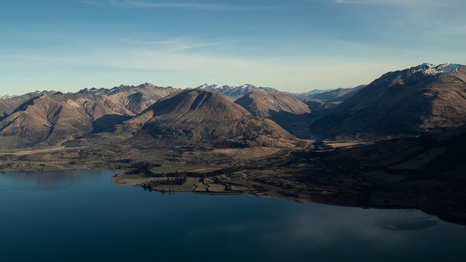 Unbeatable Queenstown Helicopter Tour: Glacier Landing and Scenic Views Review 2026 - A breathtaking aerial shot of a serene lake surrounded by majestic mountains under a clear blue sky.