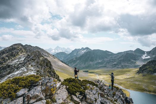 Two adventurers atop rocky mountains under a cloudy sky in a breathtaking landscape.